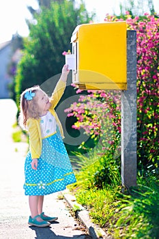 Little girl with an envelope next to a mail box