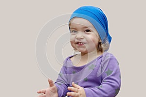 A little girl of European appearance in cap Bone smiles and claps her hands on a light background, a place for text.