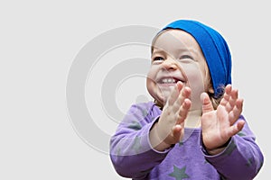 A little girl of European appearance in cap Bone smiles and claps her hands on a light background, a place for text.The concession