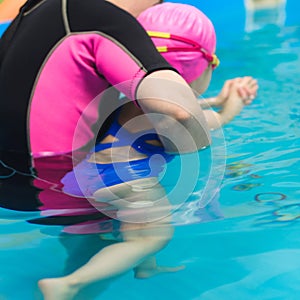 A little girl of European appearance in a pink rubber cap learning to swim in the pool