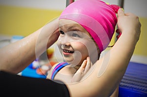 A little girl of European appearance, wearing a pink rubber swimming cap in the pool