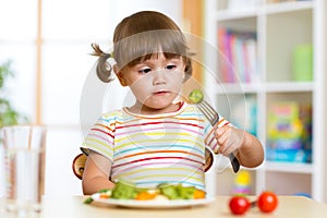 Little girl examines Brussels sprouts. Child with healthy food sitting at table in nursery