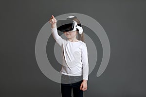 Little girl experiencing virtual reality eyeglassses in white long sleeve shirt over grey background