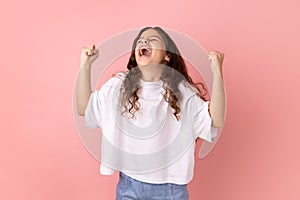 Little girl expressing winning gesture with raised fists and screaming, celebrating victory.