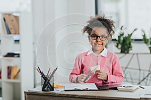 Little girl in eyeglasses holding scissors and smiling at camera