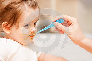 Little girl feeding from a spoon on blue chair.