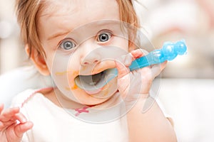 Little girl feeding from a spoon on blue chair.