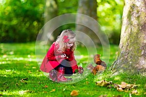 Little girl feeding a squirrel in autumn park