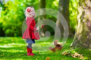 Little girl feeding a squirrel in autumn park