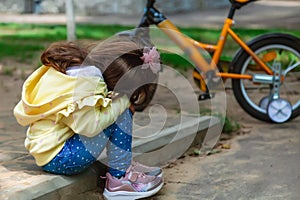 little girl fell off her bike and holds her bruised leg with her hands. sad, crying child