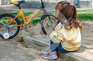 little girl fell off her bike and holds her bruised leg with her hands. sad, crying child