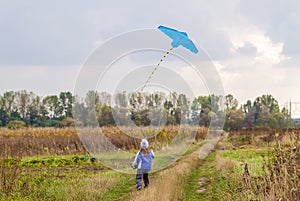 Little girl on field gravel road path running with a kite.