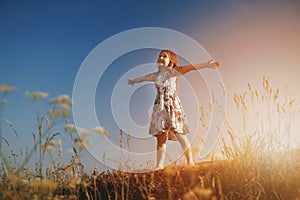 A little girl in the field with her hands up in the air