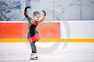 Little girl figure skater in light pink tracksuit with smile skates on the ice on an indoor skating rink