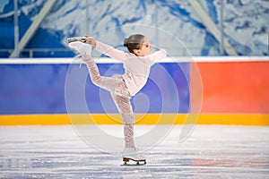 Little girl figure skater in light pink tracksuit with smile skates on the ice on an indoor skating rink