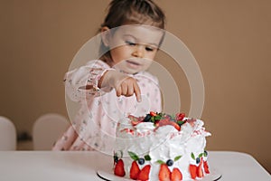 Little girl first time taste bithday cake. Cute little girl in beautiful dress tasting cake with strawberries