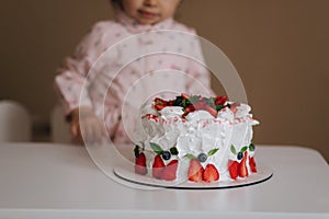 Little girl first time taste bithday cake. Cute little girl in beautiful dress tasting cake with strawberries