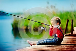 Little girl fishing from dock on lake