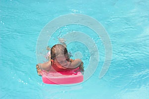 Little girl on the floating board, learns to swim in the pool