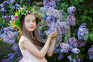 Little girl with a flower wreath on her head standing in the park on a sunny morning and smiling. Look at camera