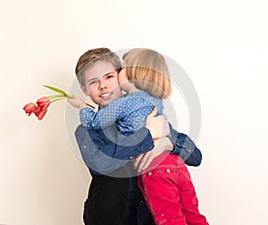 Little girl with flowers kissing her elder brother. Teen boy congratulates his little sister and gives her flowers tulips