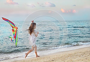 Little girl with flying kite on beach at sunset