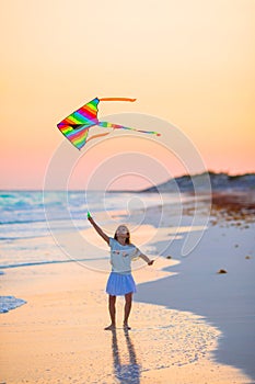 Little girl with flying kite on tropical beach at sunset. Kid play on ocean shore. Child with beach toys.