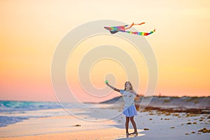 Little girl with flying kite on tropical beach at sunset. Kid play on ocean shore. Child with beach toys.