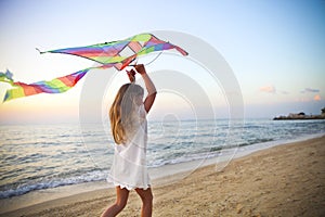 Little girl with flying kite on tropical beach at sunset