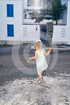 Little girl follows a rolling ball on the asphalt near the house