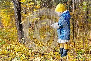 Little girl full length profile standing at yellow and orange autumn fallen leaves groundcover