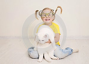Little girl in funny bee glasses and yellow t-shirt and with braids smiling happy hugging her cat