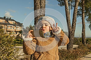 Little girl with funny kiss face and grey bonnet taking a selfie