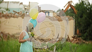 A little girl in a gas mask walks through the ruined buildings with balloons in her hand