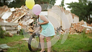 A little girl in a gas mask walks through the ruined buildings with balloons in her hand