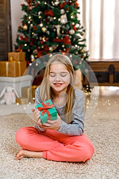 Little girl with gift box near Christmas tree on Christmas Eve at home