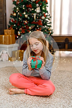 Little girl with gift box near Christmas tree on Christmas Eve at home