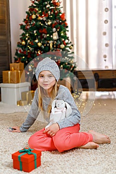 Little girl with gift box near Christmas tree on Christmas Eve at home