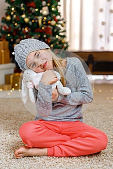 Little girl with gift box near Christmas tree on Christmas Eve at home