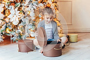 Little girl with gift box near Christmas tree on Christmas eve at home. Young kid in light bedroom with winter