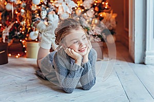 Little girl with gift box near Christmas tree on Christmas eve at home. Young kid in light bedroom with winter