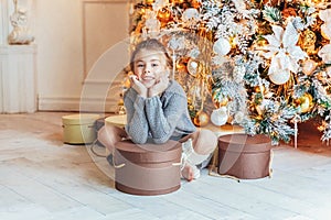 Little girl with gift box near Christmas tree on Christmas eve at home. Young kid in light bedroom with winter decoration.