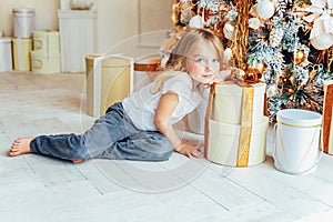 Little girl with gift box near Christmas tree on Christmas eve at home. Young kid in light room with winter decoration