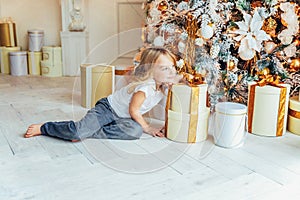 Little girl with gift box near Christmas tree on Christmas eve at home. Young kid in light room with winter decoration