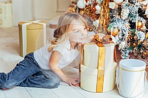 Little girl with gift box near Christmas tree on Christmas eve at home. Young kid in light room with winter decoration. Happy
