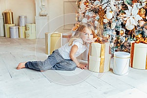 Little girl with gift box near Christmas tree on Christmas eve at home. Young kid in light room with winter decoration. Happy