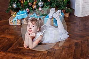 Little girl with gift box near Christmas tree at home