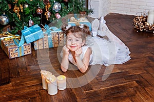 Little girl with gift box near Christmas tree at home