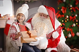 Little girl with gift box sitting on authentic Santa Claus`