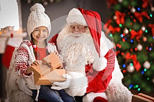 Little girl with gift box sitting on authentic Santa Claus`